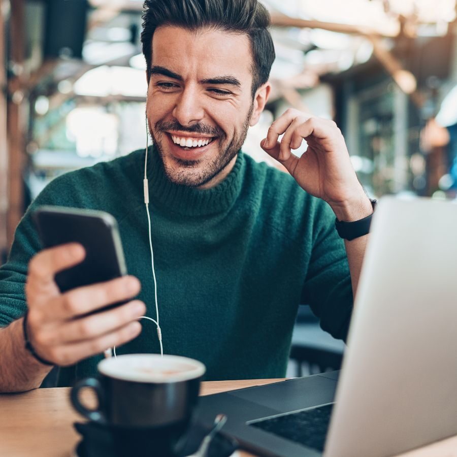 img of a man looking at a phone and a laptop